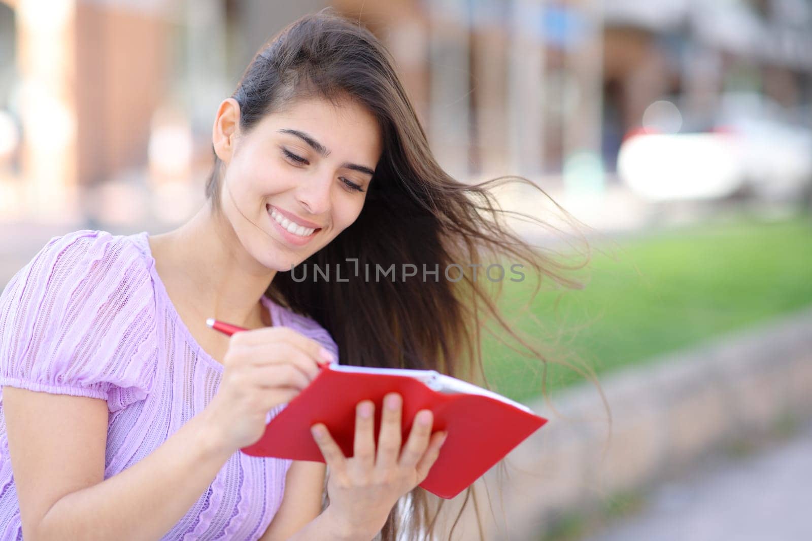 Happy woman writing in red agenda using pen in the street