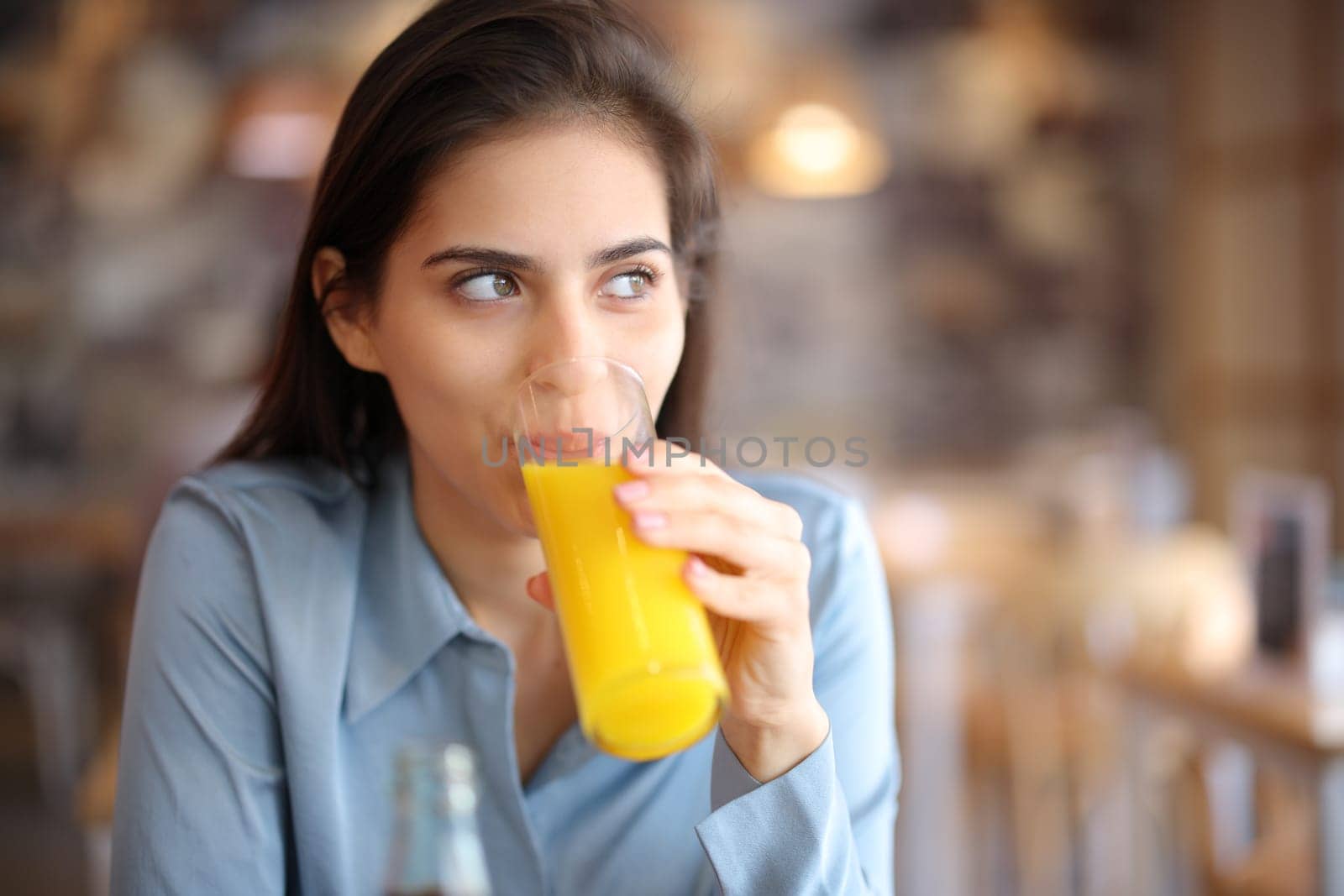 Woman distracted looking at side drinking orange juice in a bar interior