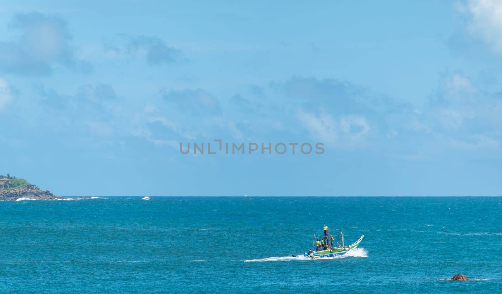 Galle Sri Lanka - September 14 2024; Local fishing boat or oruwa named Silent Heat loaded with men in bright clothes motors across bay.