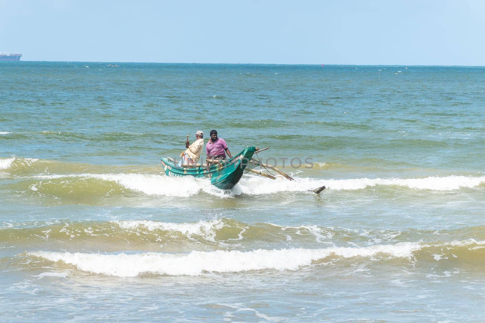 Galle, Sri Lanka - September 14 2024; Two men coming in through small surf in traditional fishing boat or 
oruwa at South Sri Lankan beach.