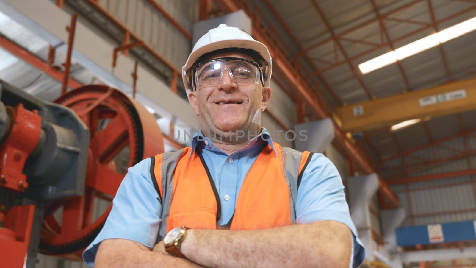 Portrait of senior man worker in safety uniform of large modern factory crossing arms on chest, Smiling and happy employee at Metal sheet stamping machine while working at industrial production plant