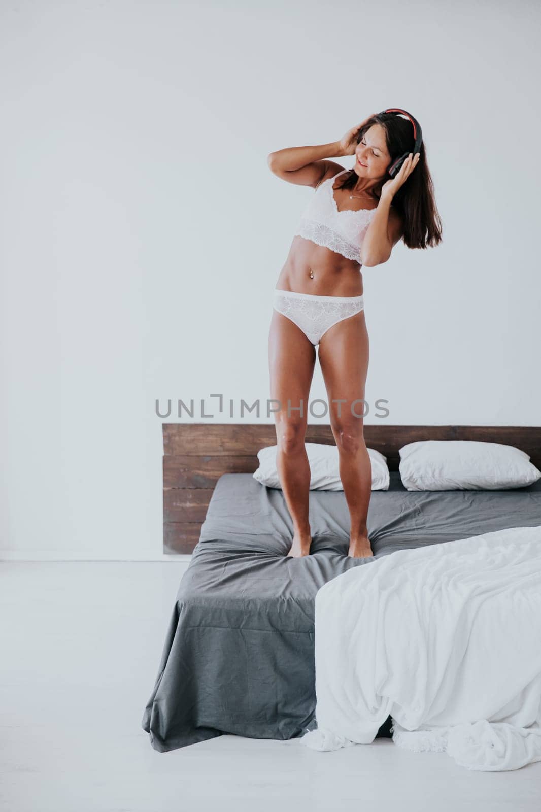 Brunette in lingerie listening to music in headphones and dancing in bedroom on bed