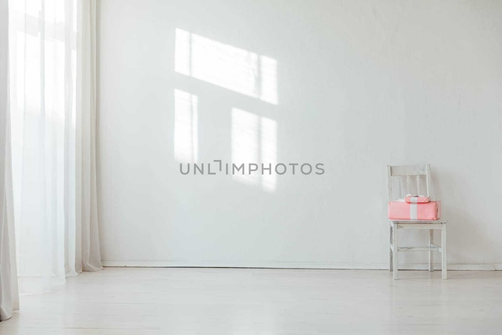 Old chair with pink gift in the interior of a white room with a window