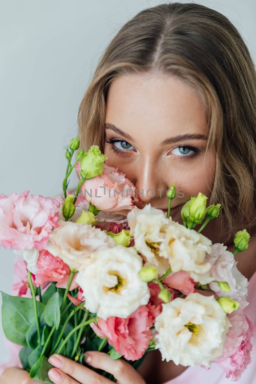 Fashionable woman in summer pink dress with bouquet of spring flowers in white room