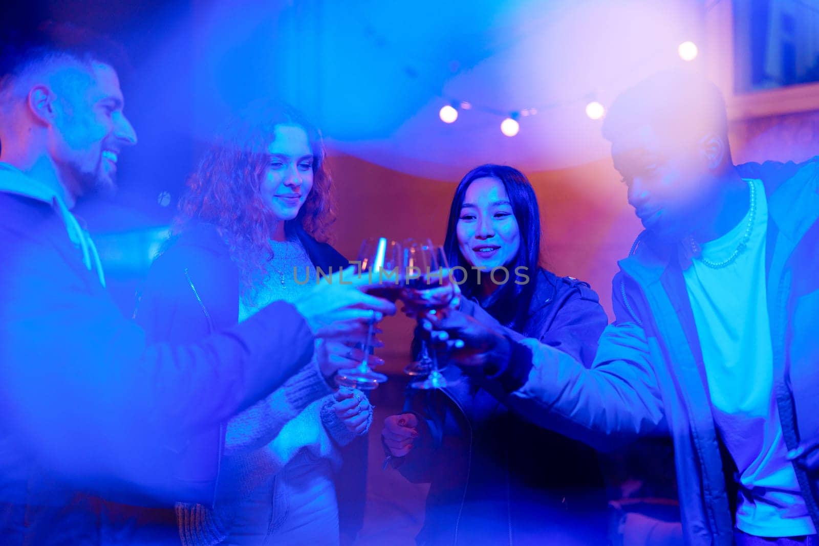 Group of friends toasting with glasses in a friendly gathering. The atmosphere is vibrant with soft lighting and cheerful chatter, creating a festive evening.