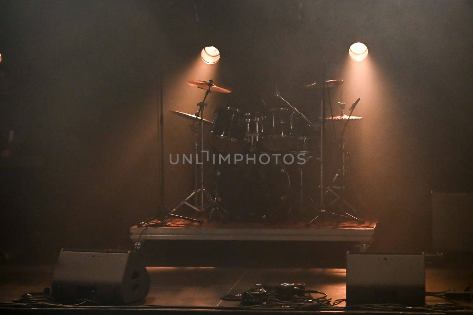 Bright stage lights illuminate the drum set as an excited crowd waits for the performance to begin, creating an atmosphere full of energy and anticipation.