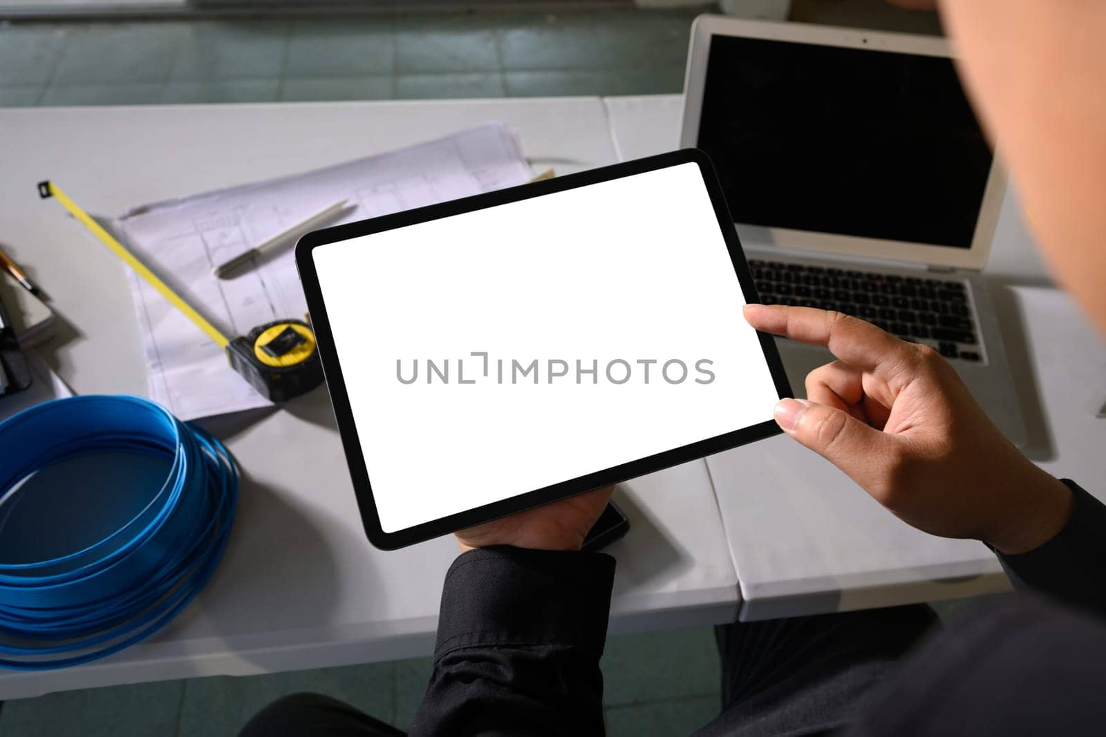 Engineer holding digital tablet with blank white screen at construction planning table.