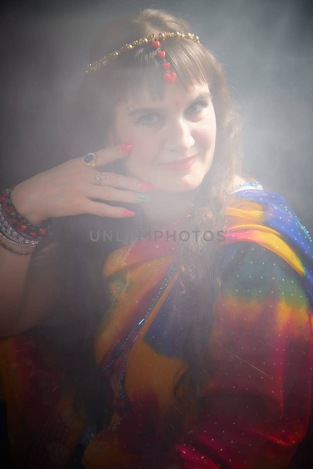 In a vibrant sari, a mature blonde woman poses elegantly, showcasing Indian attire alongside artistic smoke effects for a unique photoshoot.