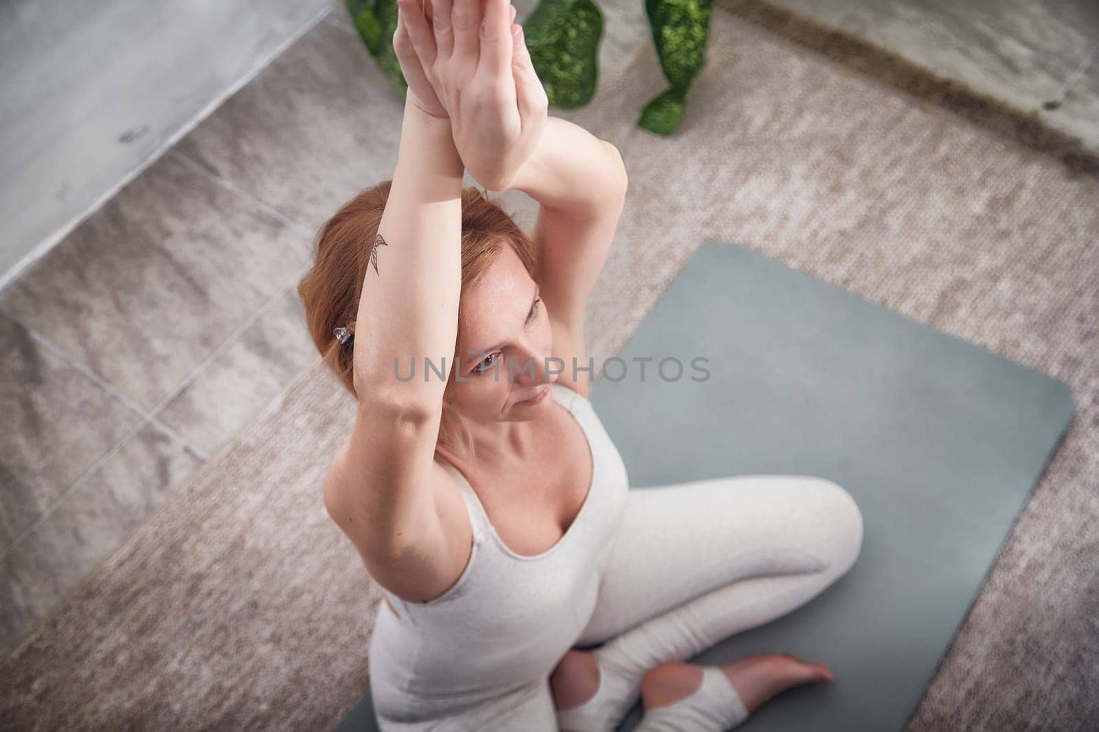 A woman practices yoga in a soothing indoor environment surrounded by greenery, embodying a commitment to health and mindfulness.