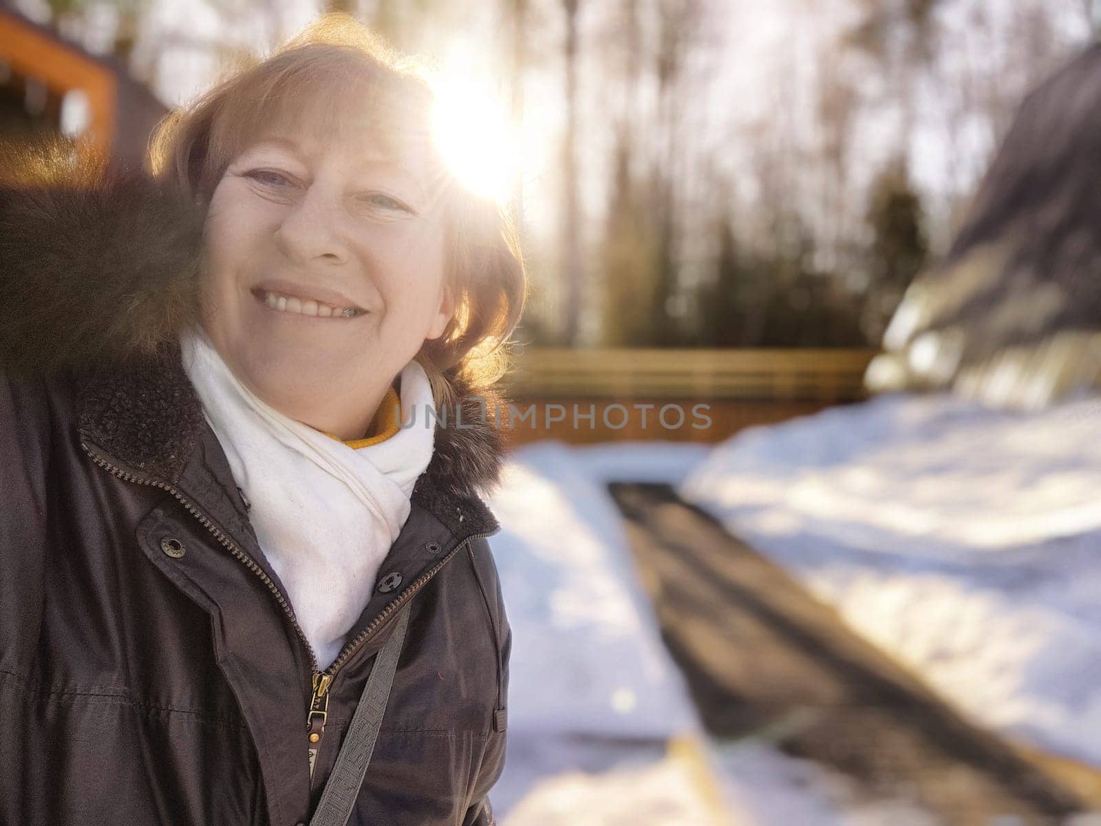 A middle aged female blogger smiles for a selfie while exploring a beautiful snowy landscape on a sunny winter day.