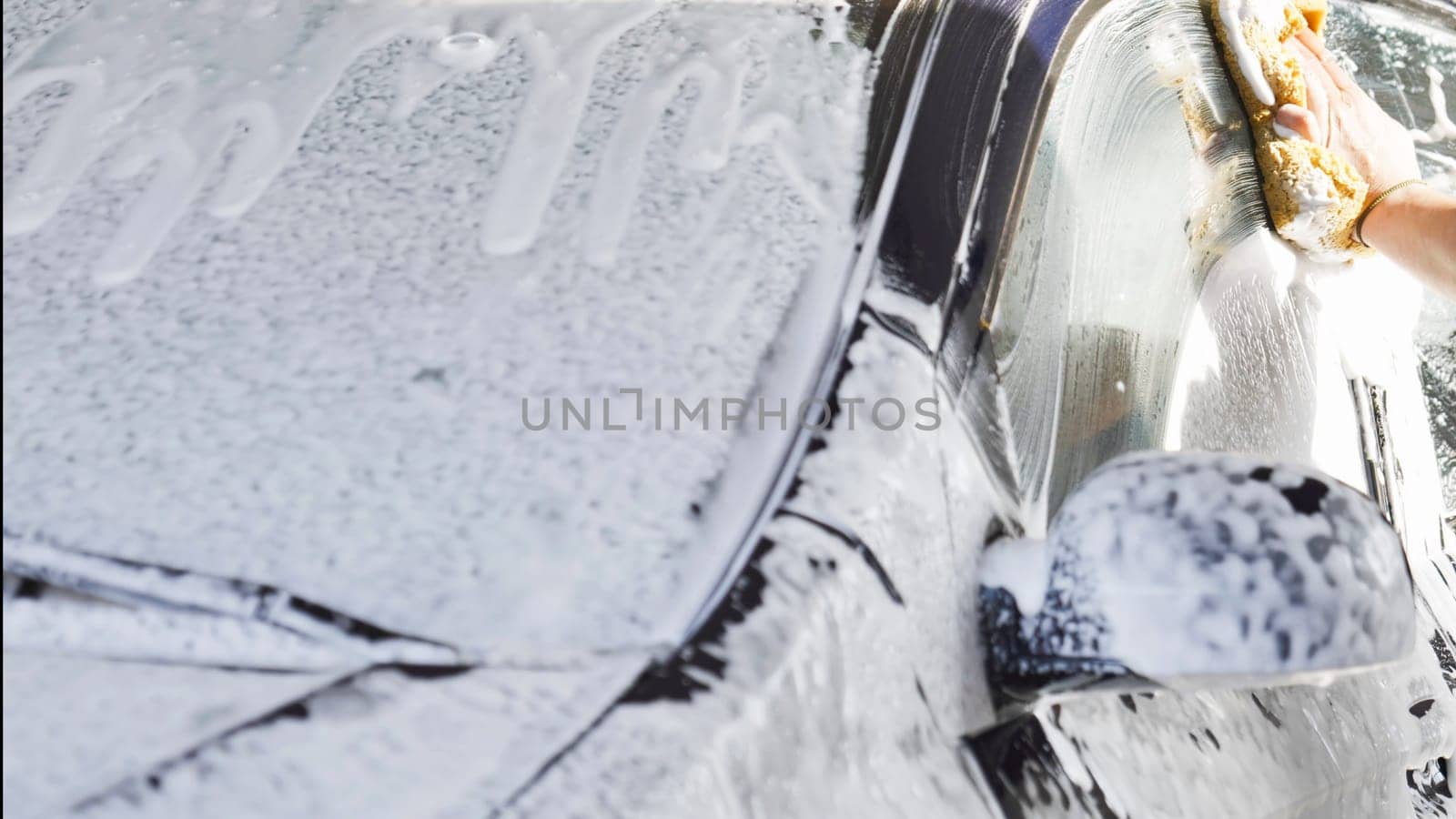Car wash worker is cleaning a vehicle with a sponge and soap