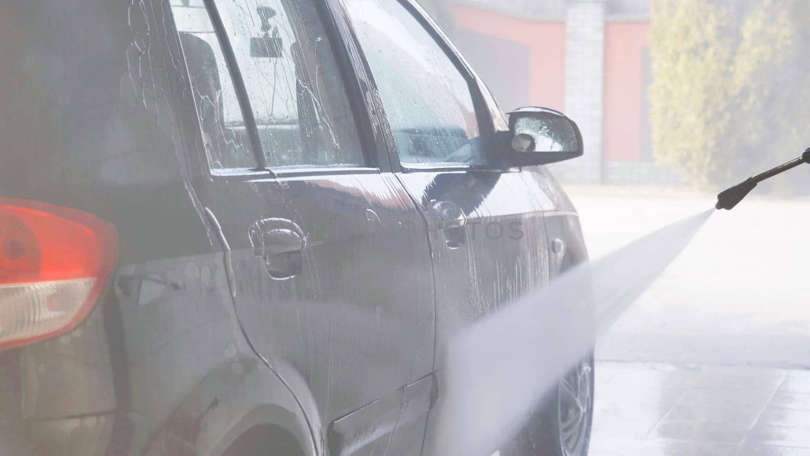 Worker washing a car with high pressure water jet in a car wash