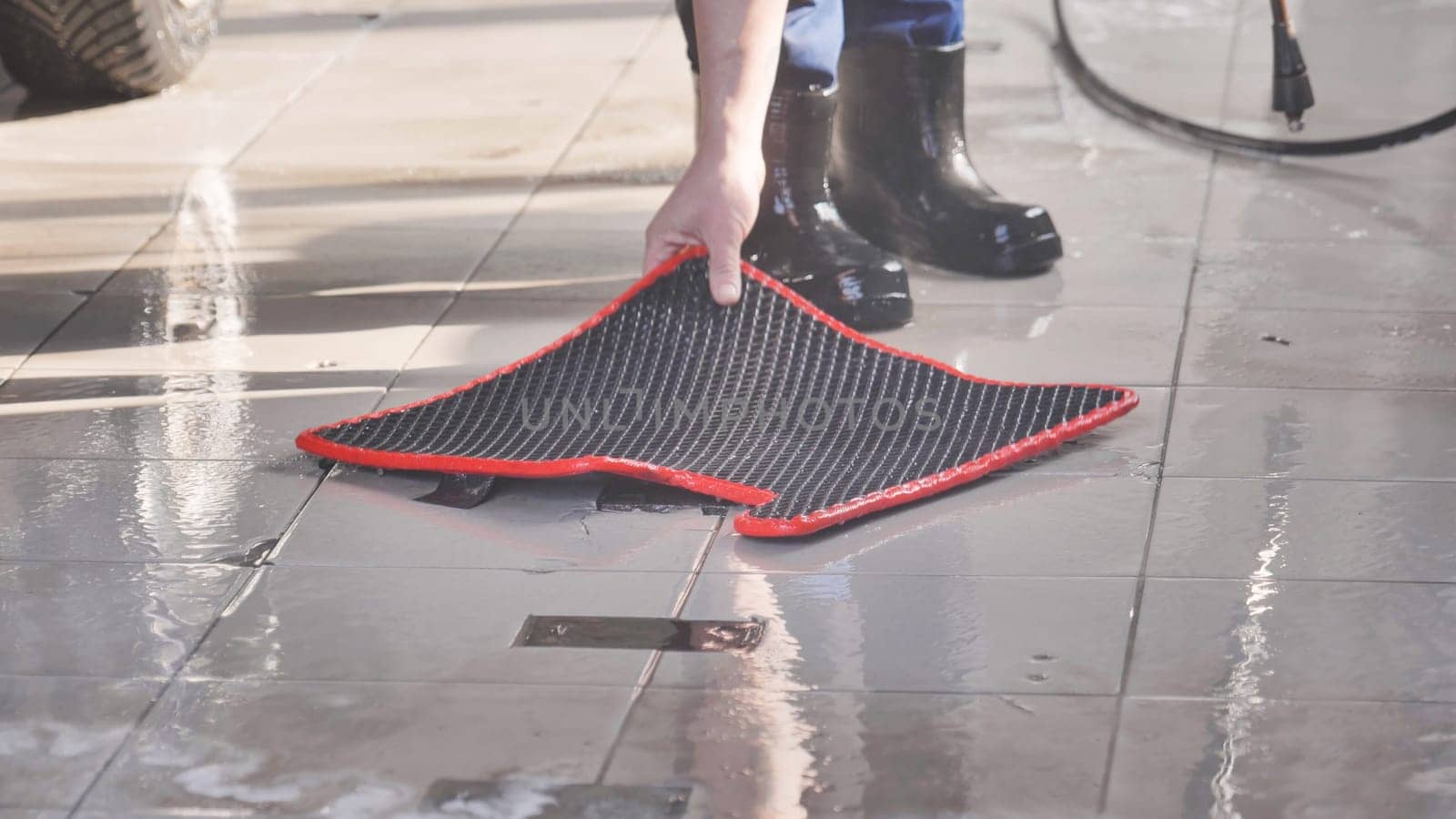 Car wash worker lifting wet car floor mat during cleaning in a professional car wash