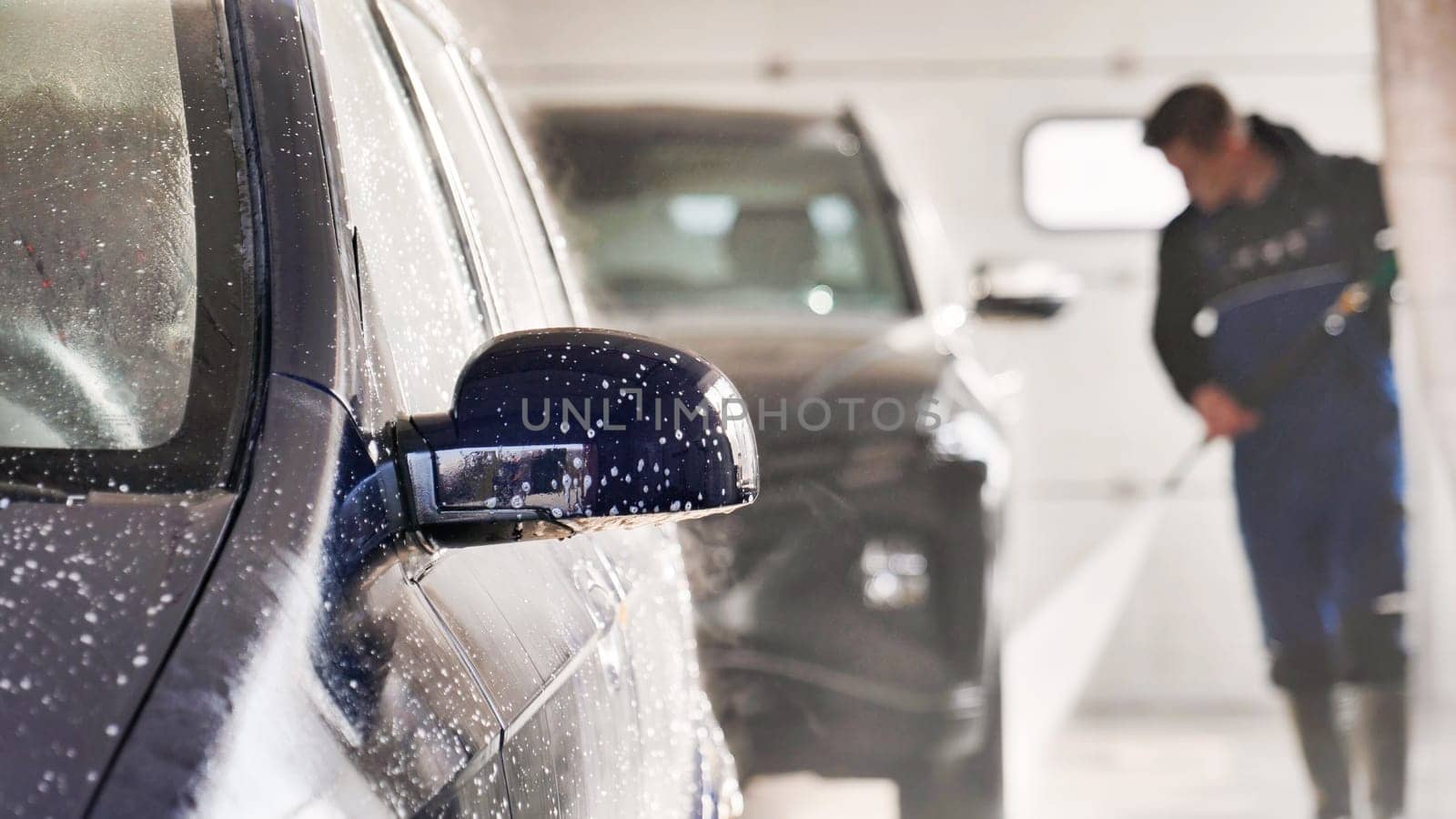 Professional car wash worker cleaning vehicle with high pressure water jet in a car wash service station
