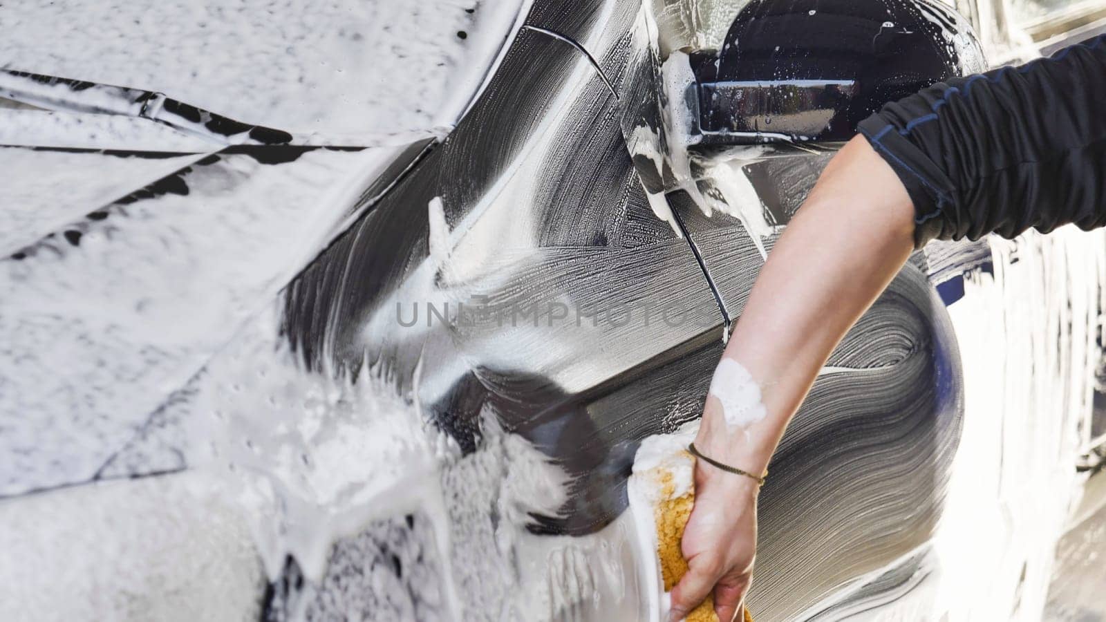Car wash worker is cleaning a vehicle with a sponge and soap foam