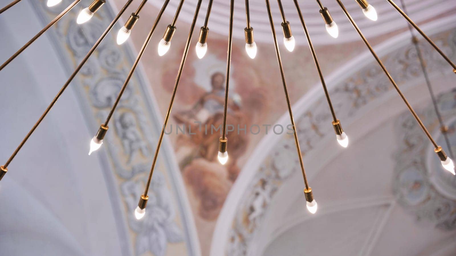 Modern chandelier illuminating ancient church ceiling with religious frescoes