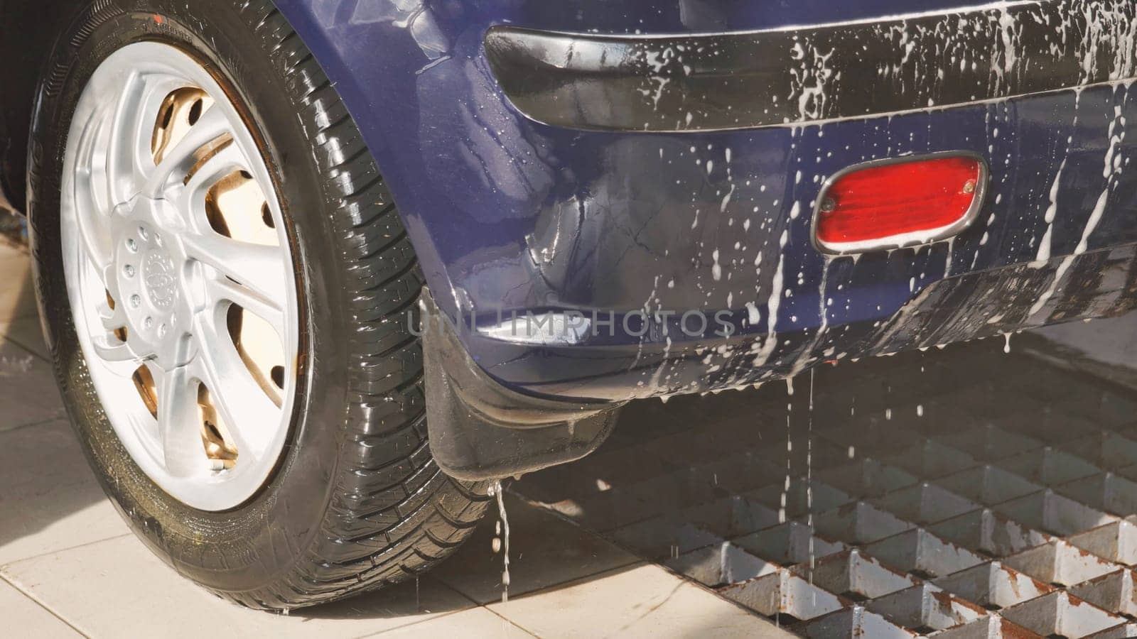 Soap dripping from the bumper of a blue car being washed
