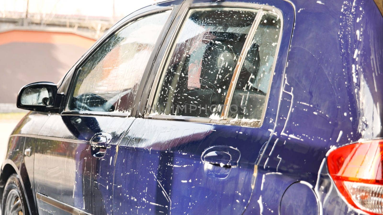 Car wash worker covering a blue car with soap during cleaning service