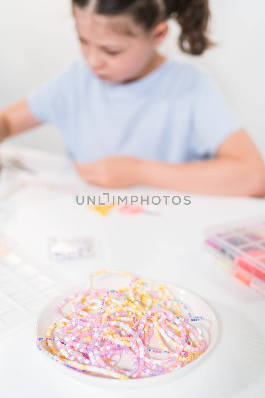 Little girl enjoys crafting colorful bracelets with vibrant clay beads set.