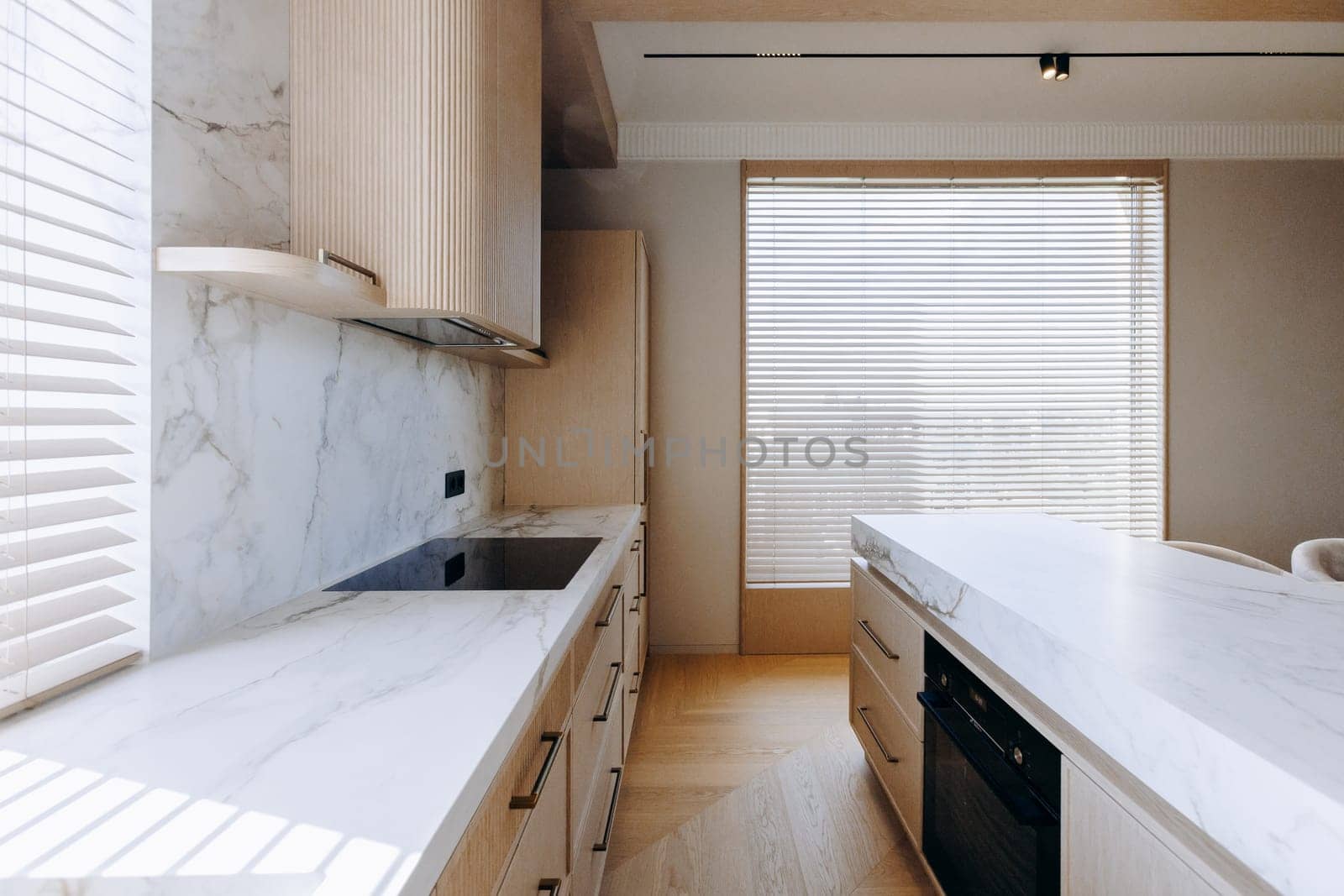 A modern kitchen featuring elegant white counter tops, stylish wooden cabinets, a spacious sink, and a large window letting in natural light