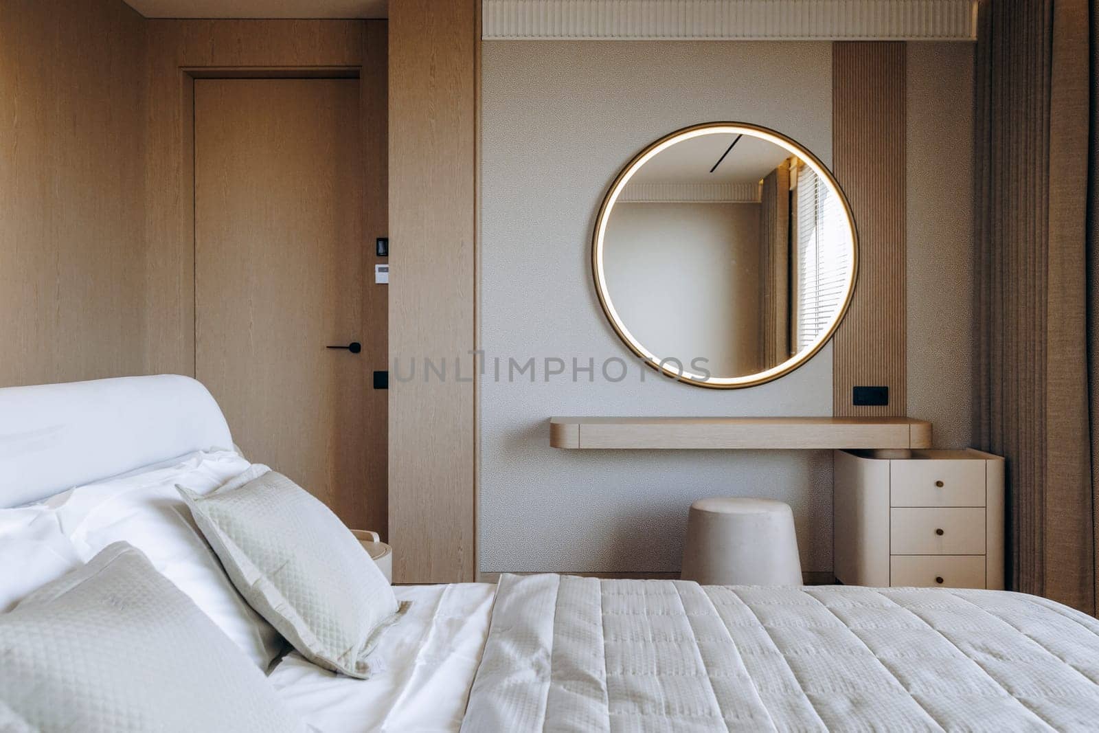 In a cozy bedroom, there is a comfortable bed adorned with soft bedding, and a stylish round mirror elegantly hanging on the wall