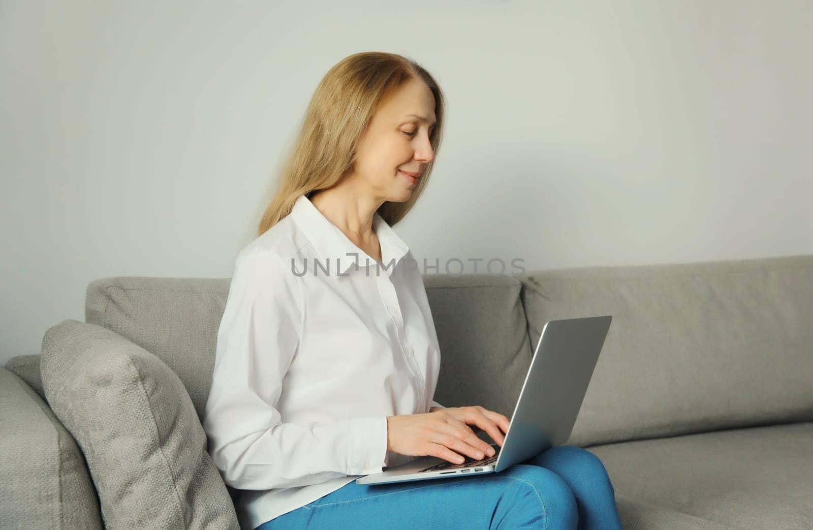 Happy modern woman working with laptop, freelancer girl looking at computer sitting on a couch in the living room at home