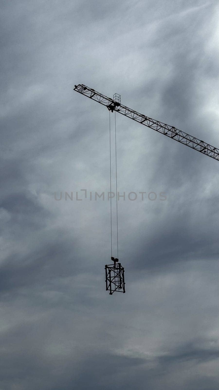 Budva, Montenegro - April 18, 2025: Construction crane hoisting materials against a backdrop of a dramatic sky, symbolizing the essence of building and development