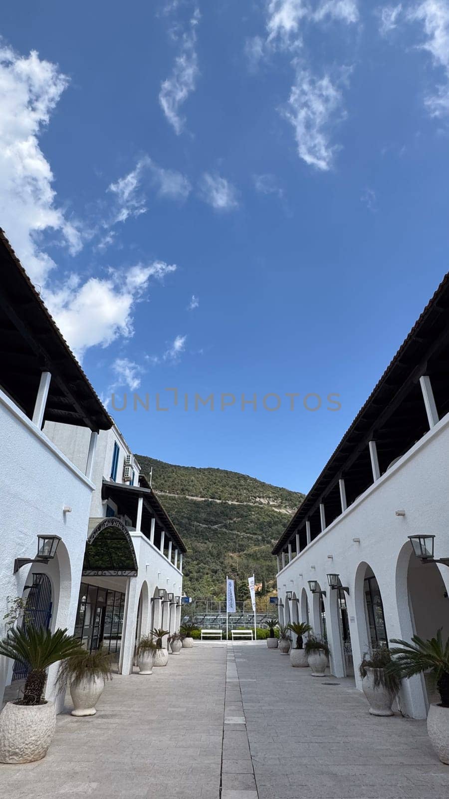Budva, Montenegro - April 17, 2025: View of the elegant white buildings of the Hotel Aleksandar with arches framed by a serene mountain landscape and clear sky.Budva Riviera