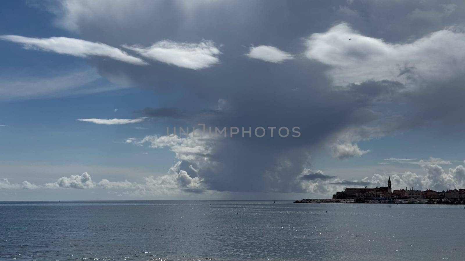 A coastal landscape with dramatic clouds over calm waters that reflect the old town, highlighting the beauty and serenity of nature