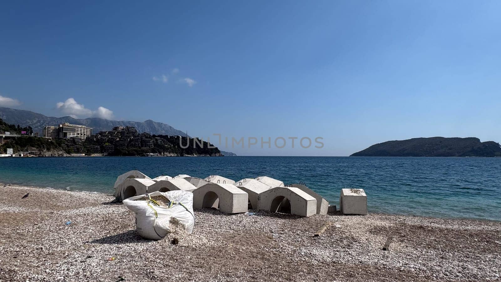 Budva, Montenegro - April 17, 2025: Coastal landscape with stone details for fortification on the beach and a torn bag with pebbles inside