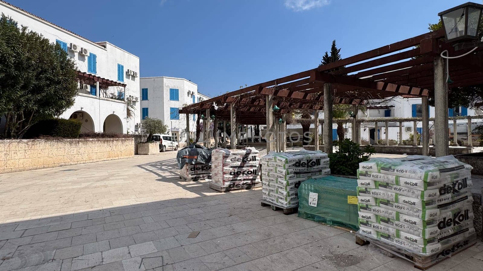 Budva, Montenegro - April 17, 2025: Square with empty cafes near the VILA CANA building, next to which are building materials piled up and white buildings in the distance