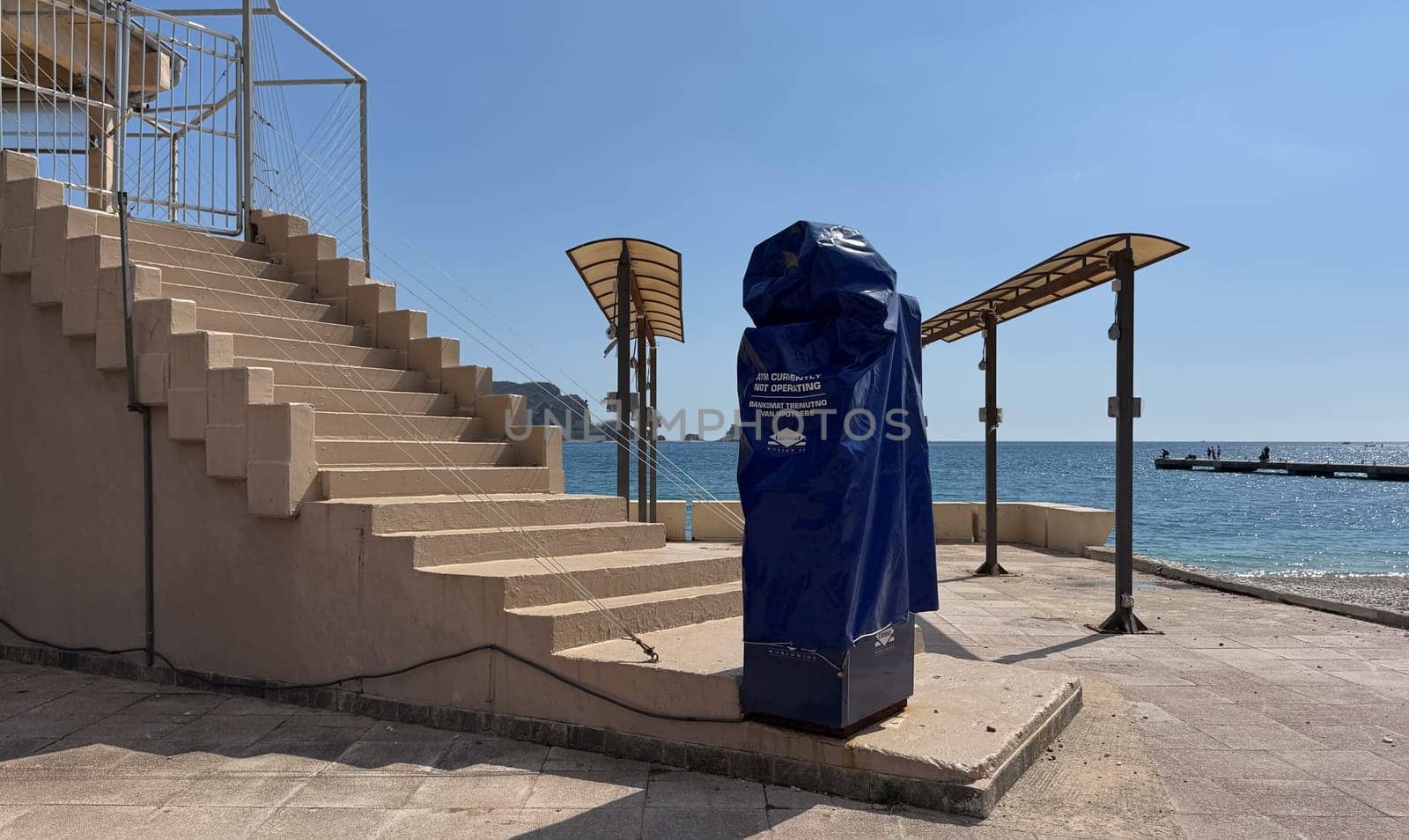 Budva, Montenegro - April 17, 2025:An ATM, covered with a cover for the winter period, stands on the embankment near a cafe