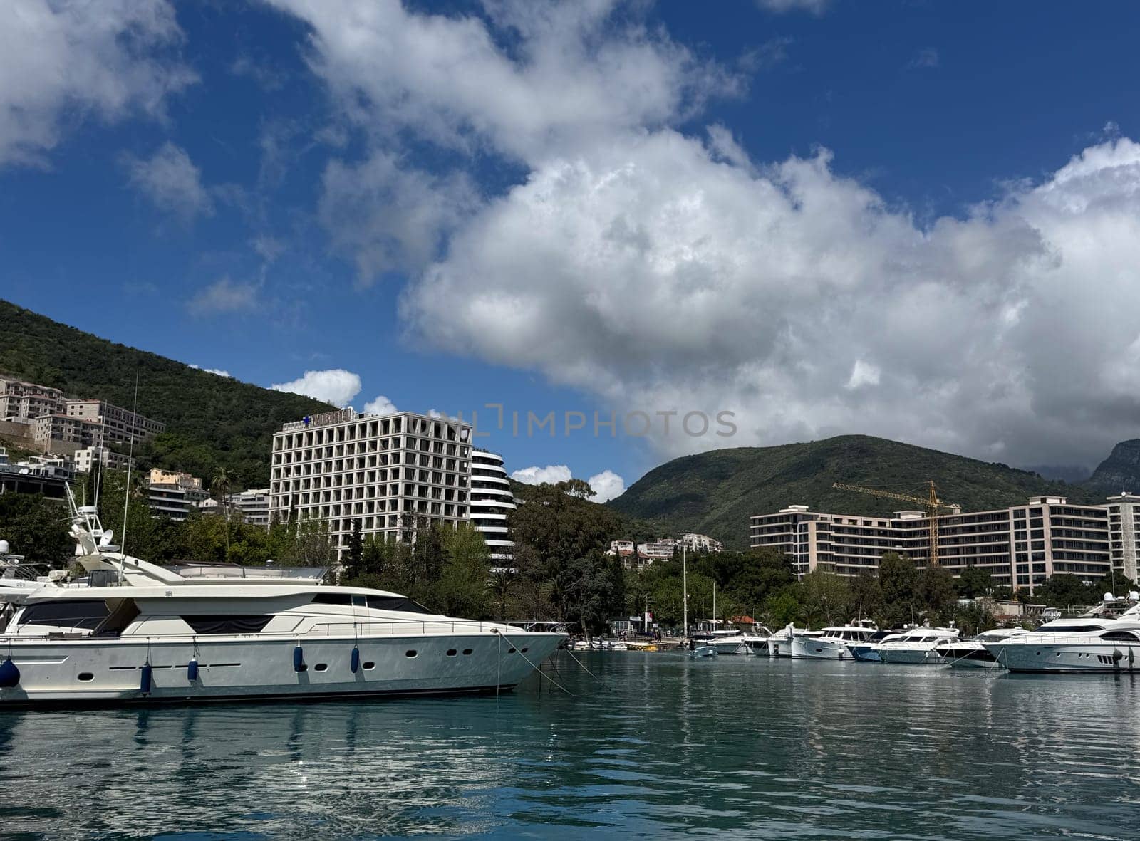 Budva, Montenegro - April 18, 2025: A marina with luxury yachts and modern buildings set against a picturesque coastal landscape