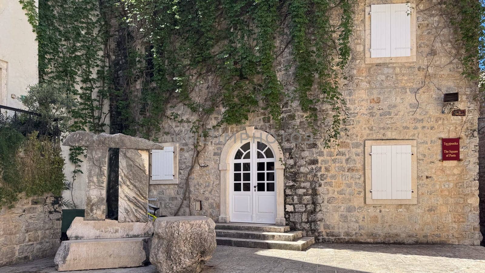 Budva, Montenegro - April 18, 2025: Historic stone building on Poets Square in the Old Town, decorated with greenery and sculptures