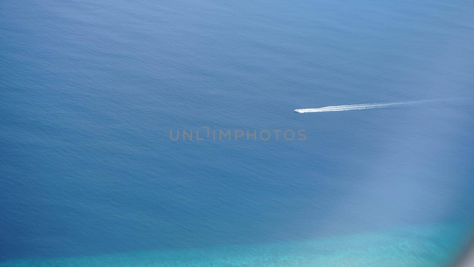 Speedboat gliding across deep blue waters, leaving a striking white trail behind. Aerial view captures the small boat navigating the ocean above a vibrant turquoise seabed