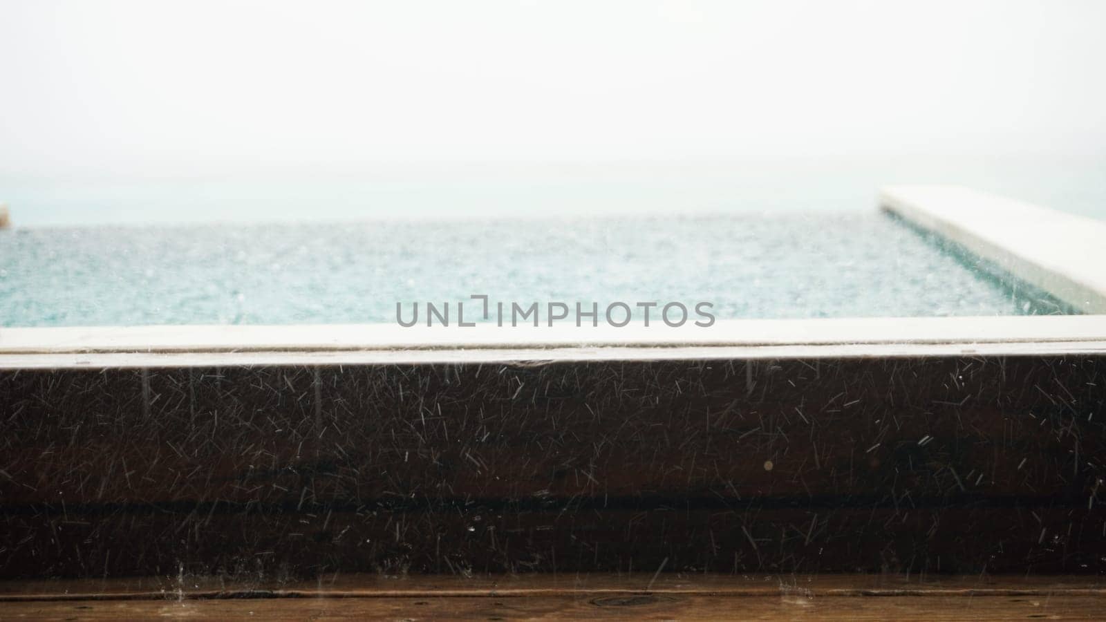 Rain cascading on an infinity pool overlooking the ocean creates a serene and moody atmosphere during a stormy day, enhancing the tranquil beauty of the seascape