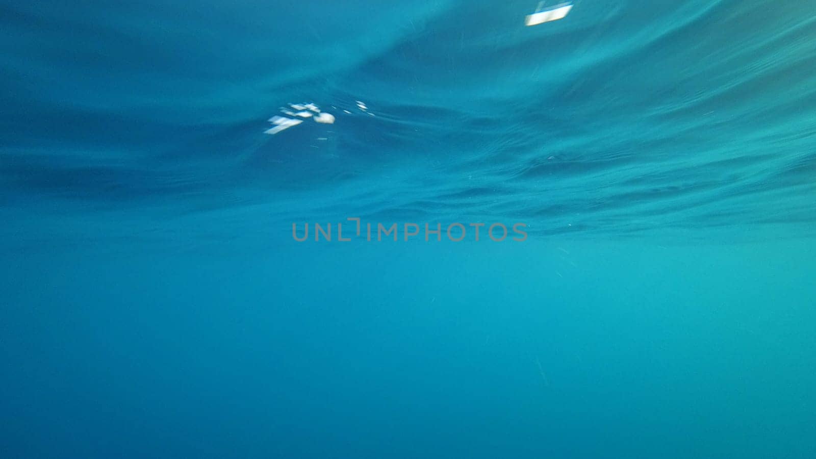 Sunlight filtering through the rippling surface of a tranquil turquoise ocean creates a mesmerizing underwater scene, perfect for evoking a sense of serenity and wonder