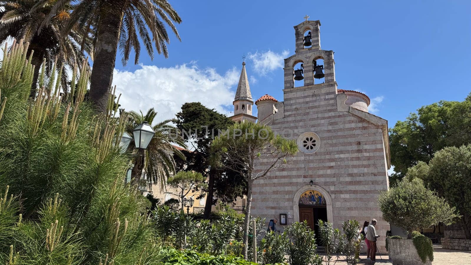 Budva, Montenegro - April 20, 2025: Easter celebrations take place in the historic Church of the Holy Trinity in the Old Town, surrounded by palm trees and lush greenery