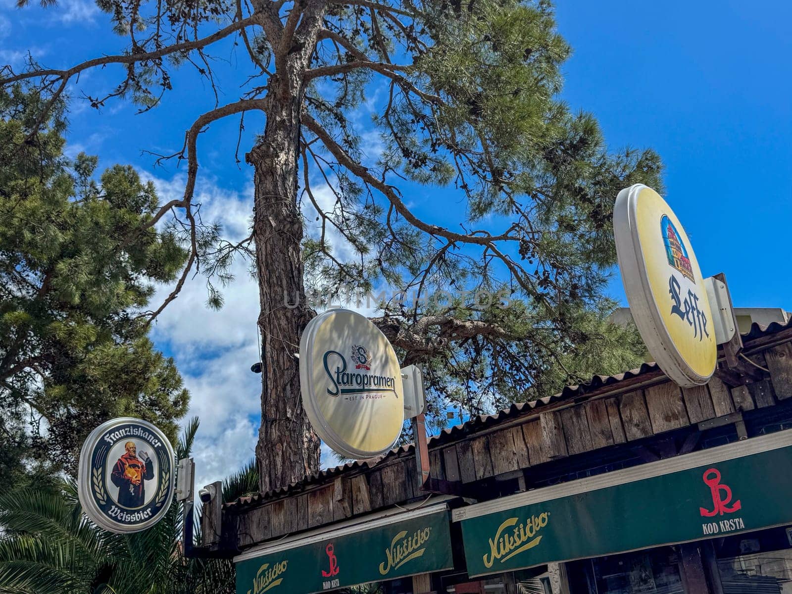 Budva, Montenegro - April 18, 2025: Staropramen, Niksicko, Franziskaner Weissbier brand name on the canopy of the KOD KRSTA bar under the tree