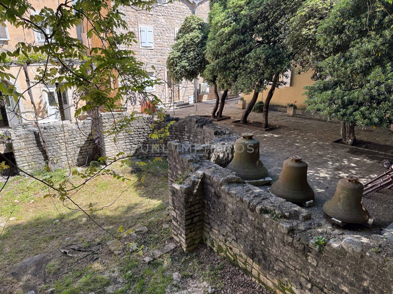 Budva, Montenegro - April 18, 2025: Historic courtyard with ancient bells and lush trees in the Old Town. Concept Cultural Significance and History