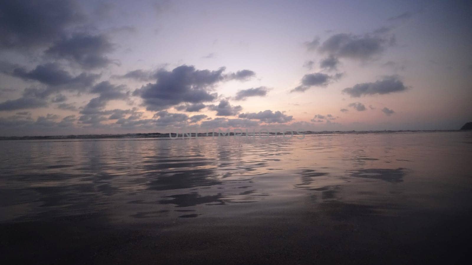 Calm ocean waves reflecting golden sunset light dance beneath a stunning cloudy sky, creating a tranquil and serene atmosphere perfect for evening relaxation