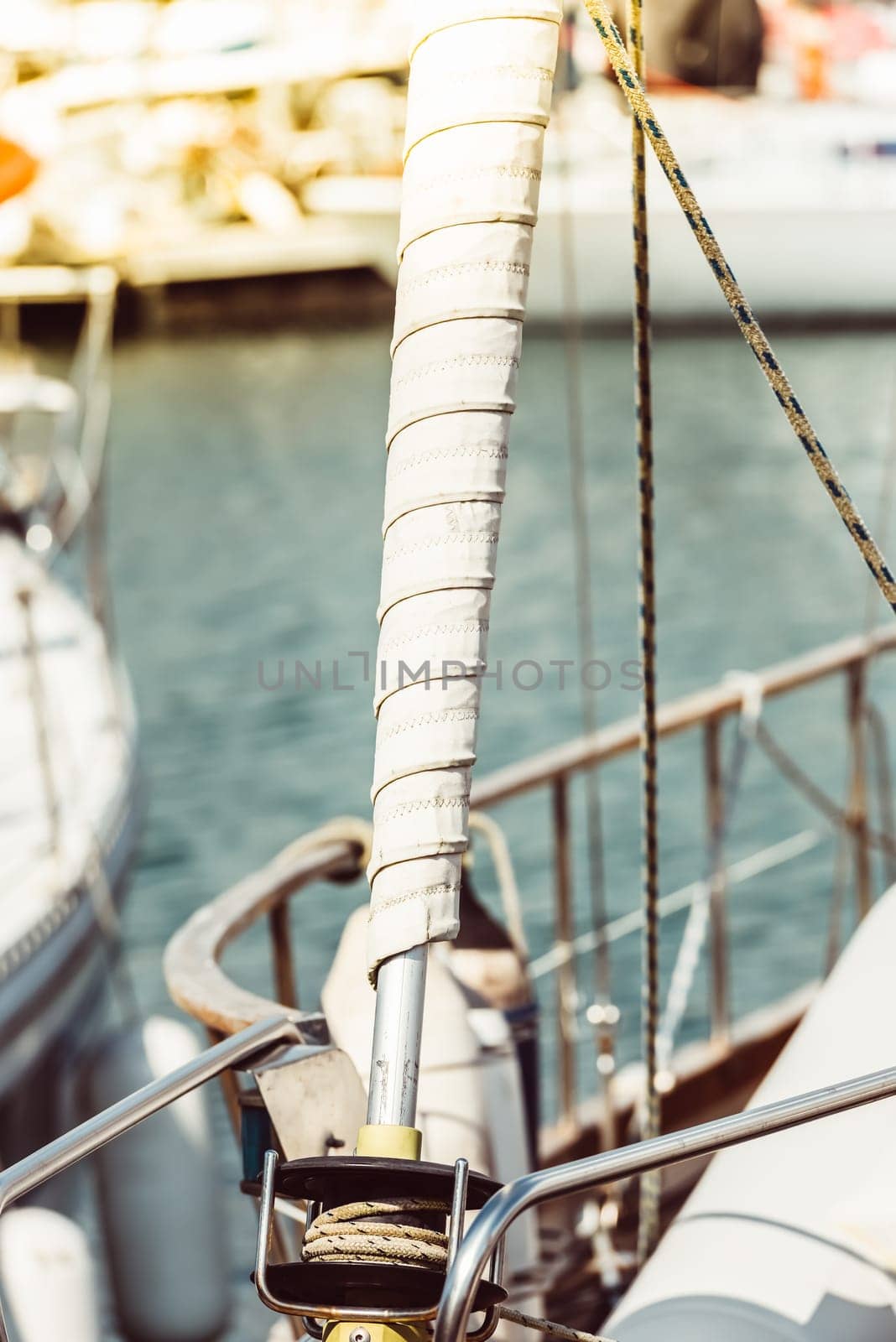 Sailboat mast with wrapped sail detail in marina setting, ideal for nautical background