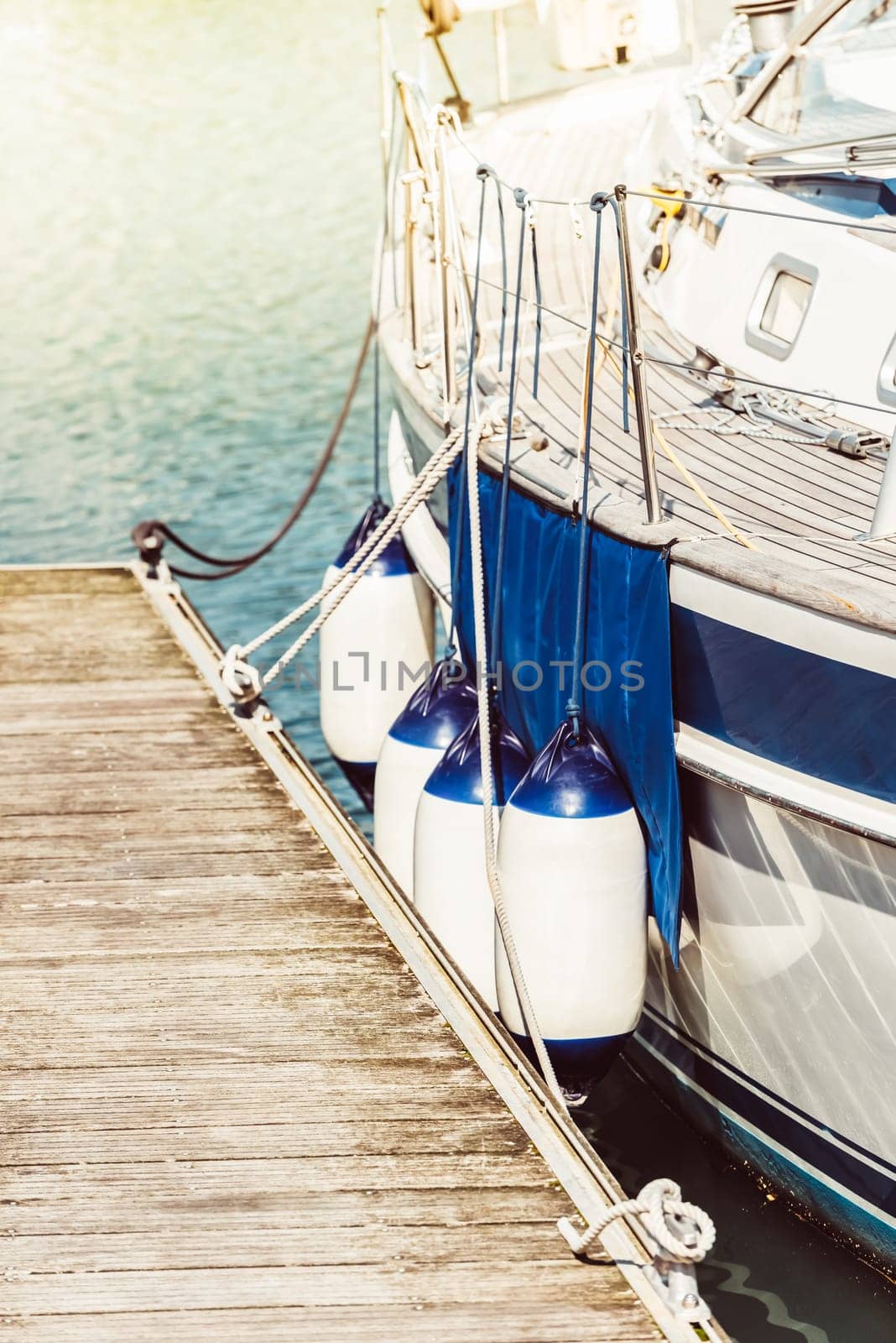 Boat docked by wooden pier with blue fenders and calm water, background