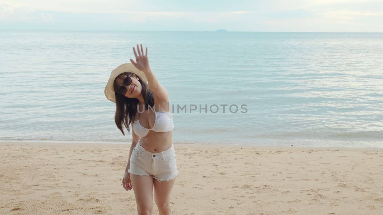 Beautiful Asian woman wear sungrass and hat turning back running to tropical paradise beach, Happy female in bikini having fun with hand to camera inviting you come with me