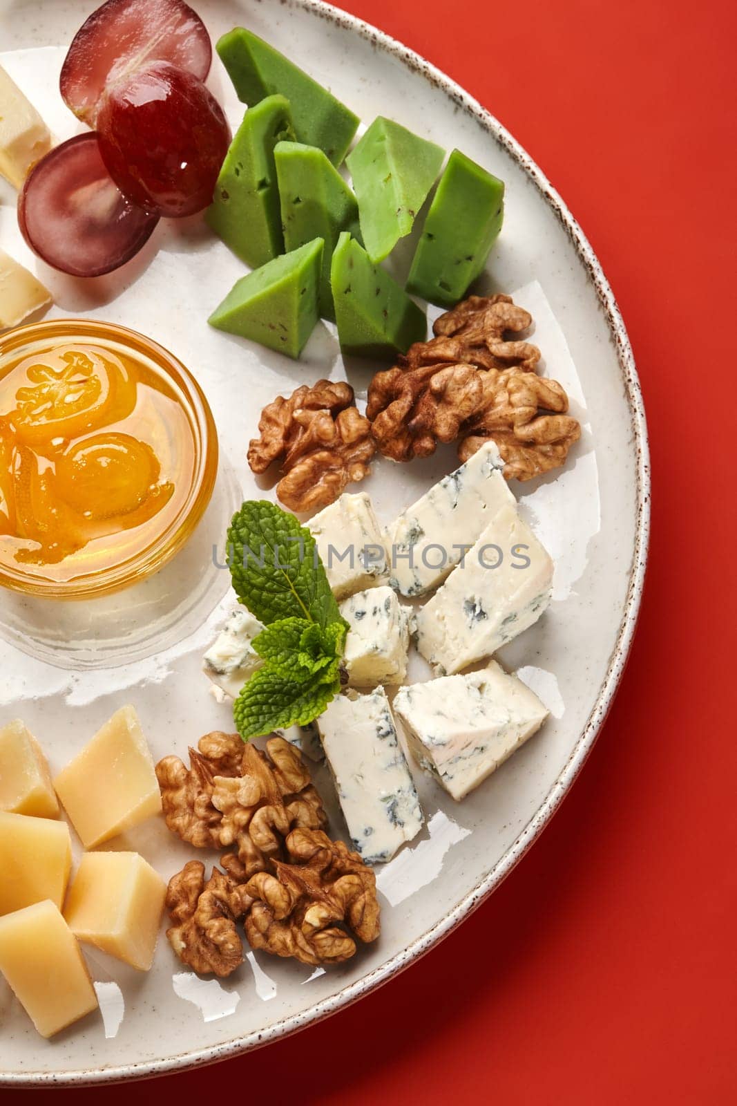 Delicious cheese plate with various types of cheese, walnuts, grapes, honey, and mint, creating a flavorful and visually appealing culinary experience