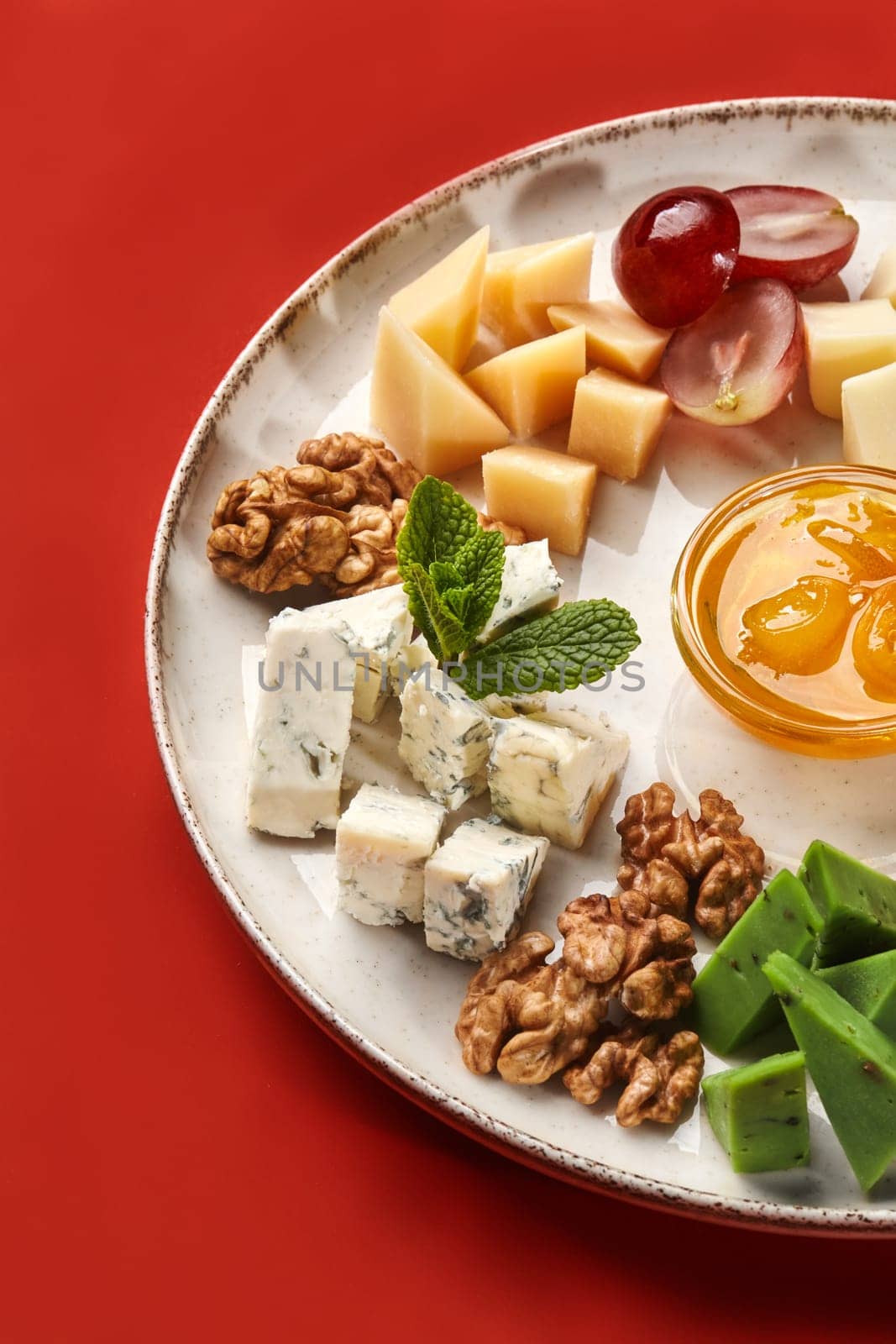 Different types of cheese with nuts, grapes and honey on a plate on a red background