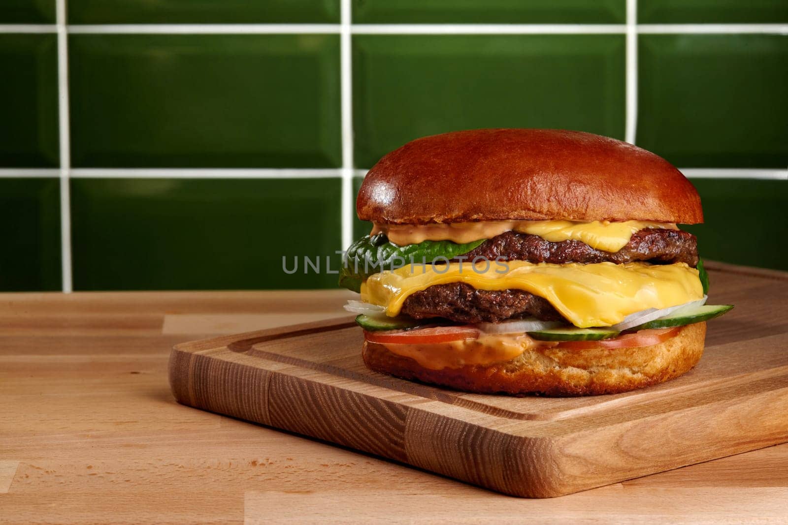 Tasty cheeseburger with melted cheese, lettuce, tomato, and sauce is waiting to be eaten