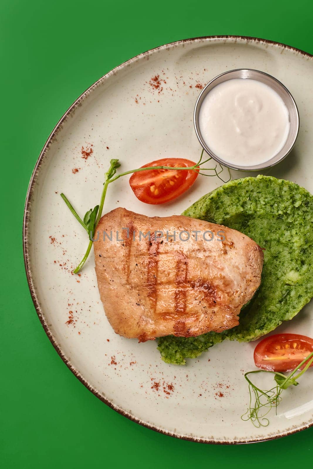 Delicious grilled chicken breast served with spinach puree, cherry tomatoes, white sauce, and microgreens on a plate