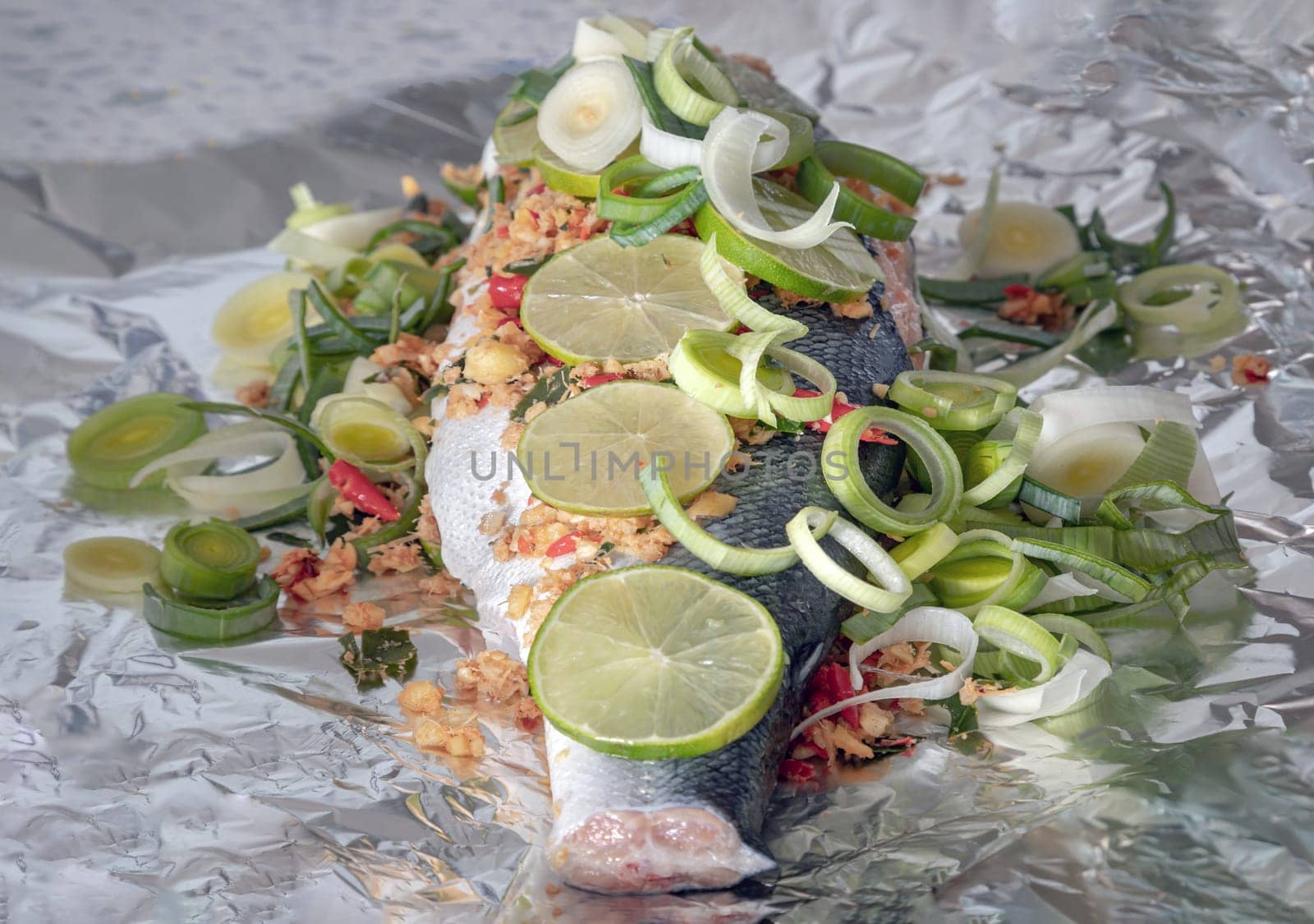 Prepare Whole Baked Salmon with Herbs on aluminium foil. ingredient include Coriander root, Ginger, Galangal, Kaffir lime, Leek, chopped together and Bird's eye chili with Slice lemons place on the Salmon fish. Healthy eating, use it as your Wallpaper, Poster and Space for text, Selective focus.