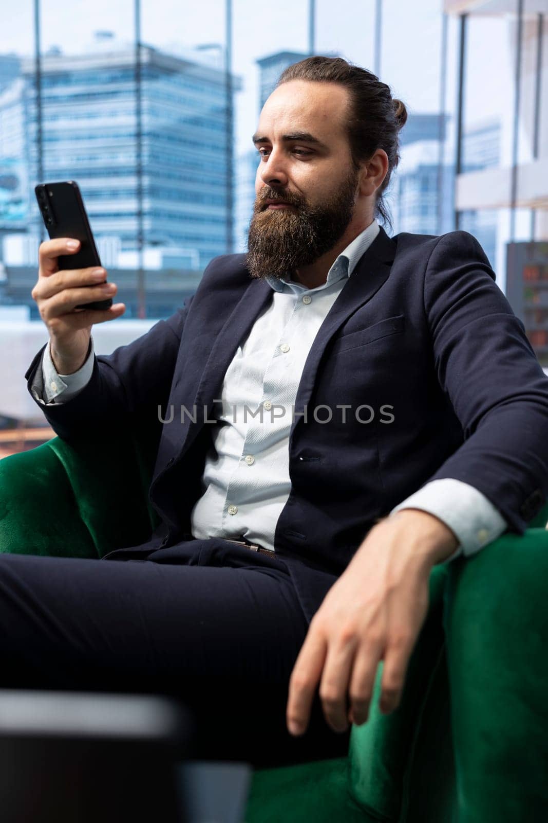 Influential businessman CEO navigating on his smartphone at the office, setting his objectives for productivity and efficiency. Young entrepreneur leads a corporation, multitasking.
